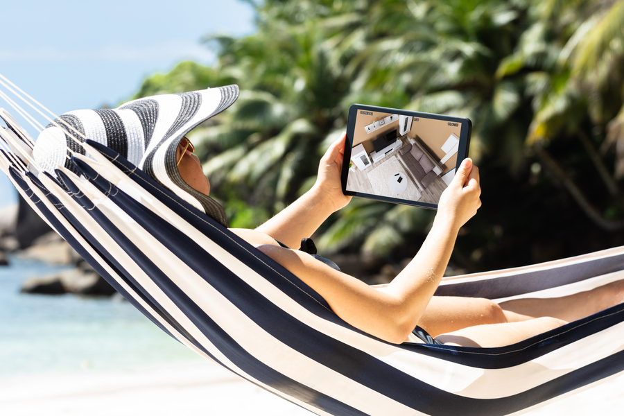 <p>Person relaxing in a hammock while monitoring home security cameras on a tablet.</p>